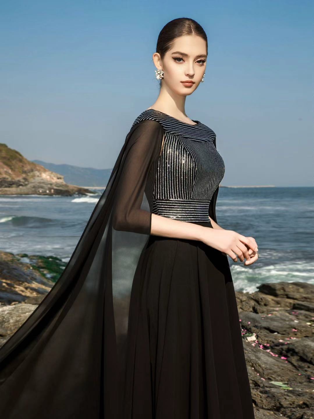 Vestido longo preto com aplicações manuais fotografado à beira-mar